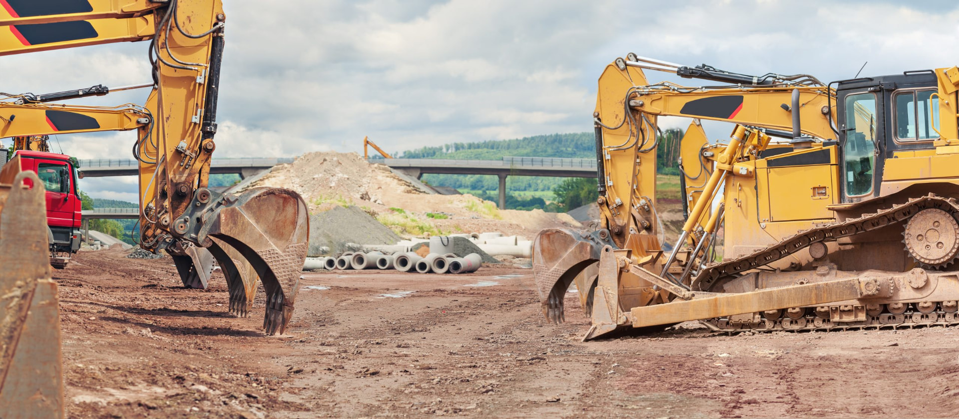 Excavators and a dozer on a construction site with concrete pipe staged for installation
