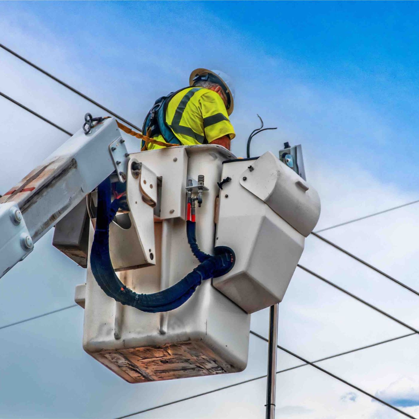 Lineman in a hard hat and safety vest working from a bucket truck among overhead power lines