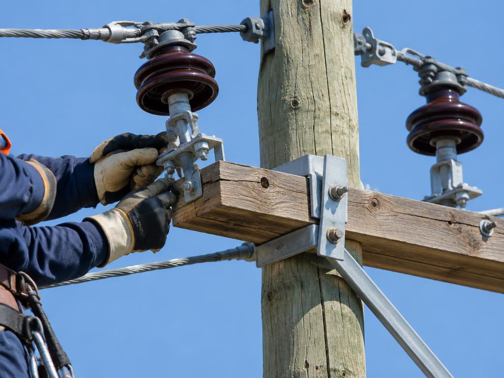 Gloved lineman fastening an insulator on a utility pole crossarm